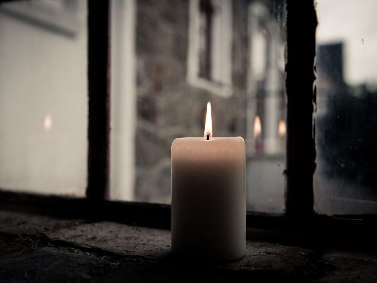 Brennende Kerze an einem Fenster in der Dämmerung